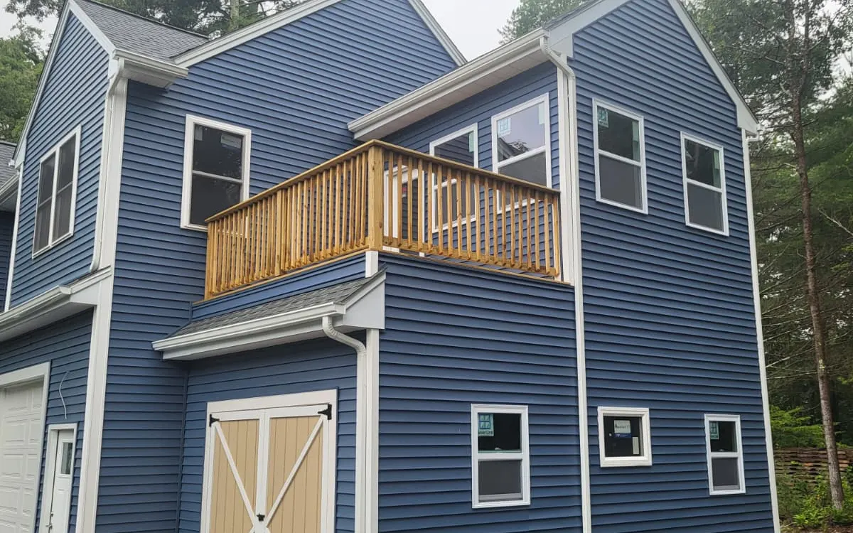 Side view of a new garage ADU with blue siding, barn-style doors and an upper balcony