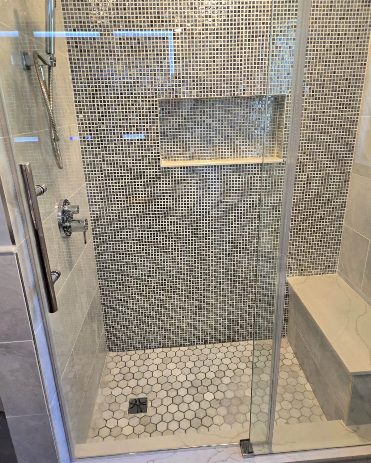 Walk-in shower with mosaic tile walls, built-in bench, niche and frameless glass