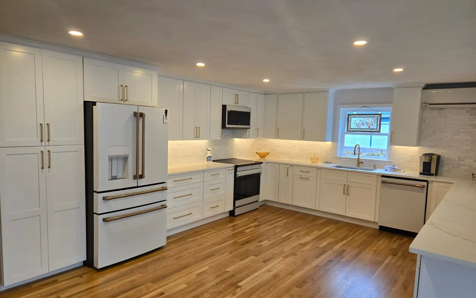 Open white kitchen with quartz counters, hardwood floors and under-cabinet lighting