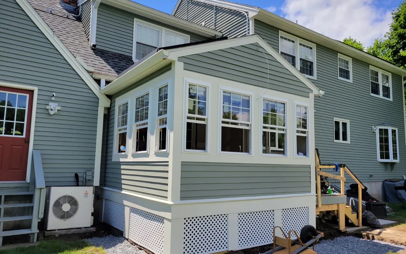 Sunroom addition with wraparound windows and green siding on a New England home