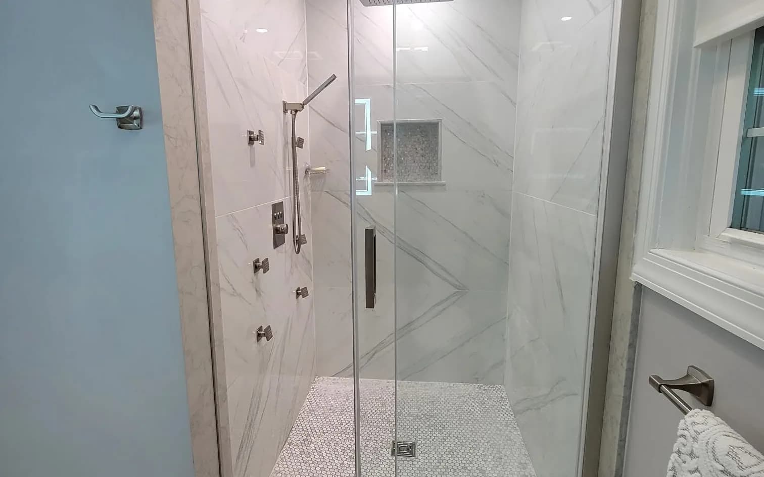 Walk-in glass shower with marble-look tile in a remodeled bathroom